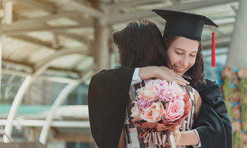 School graduate in cap & gown hugging family member